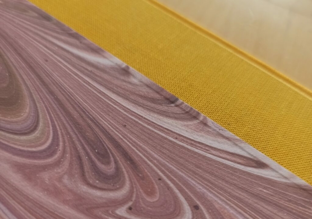 gros plan du détail de couvrure d'une reliure bradel, toile jaune, papier marbré rose